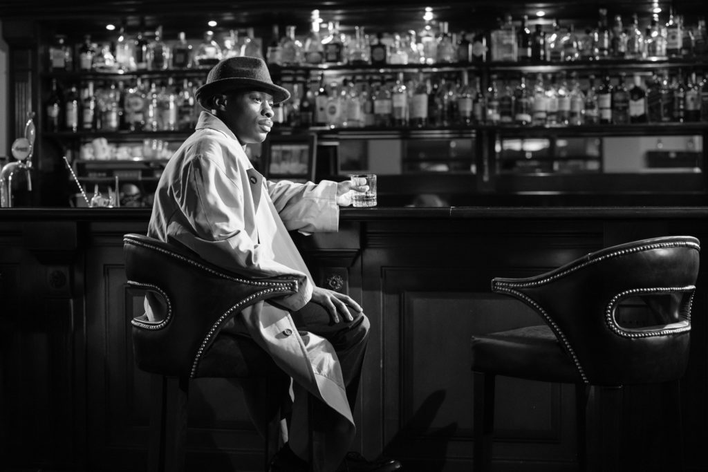 Photo en noir et blanc, un homme est assis dans un bar déco et ambiance typique des années 50