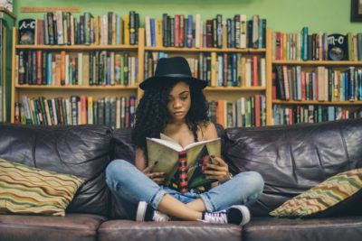 Jeune femme lisant un livre confortablement installée dans un canapé club en cuir 