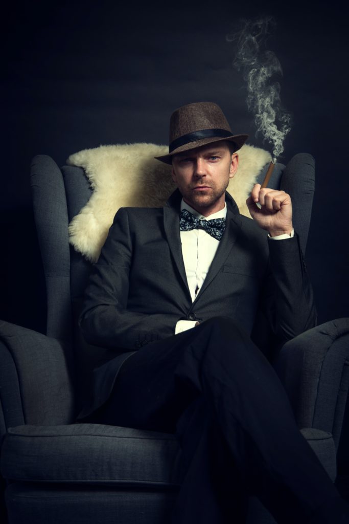 Un homme élégant fumant un cigare est assis sur un fauteuil
