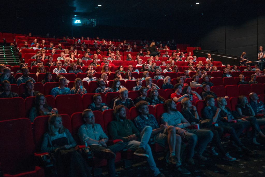 Salle de cinéma classique, spectateurs installés sur fauteuils en velours rouge 