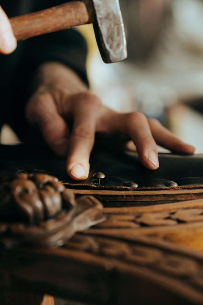 zoom sur les mains d'un ébéniste qui applique des clous de tapissier sur un fauteuil en cuir