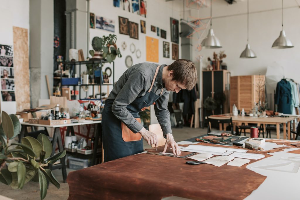 Un tapissier dans un grand atelier est penché sur sa table de travail et examine une grande pièce de cuir