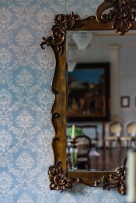 Papier peint bleu clair avec motifs fleuris symétriques blancs et miroir ancien doré qui reflète un salon anglais