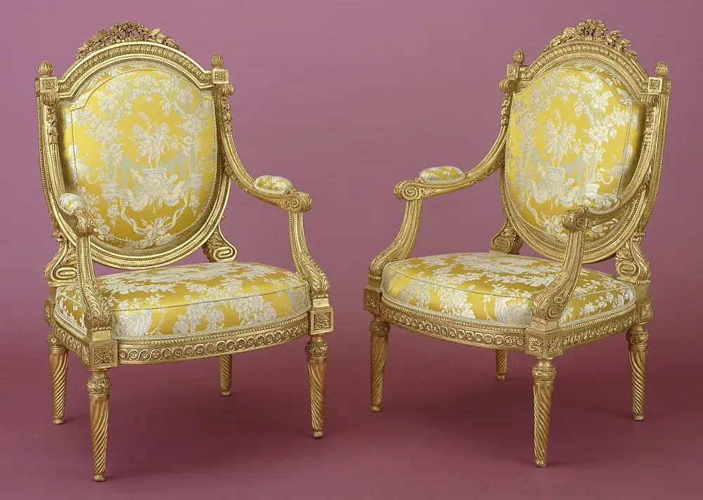 Deux sièges Louis VX avec sa structure recouverte de feuilles d'or et le dossier et assise rembourrées et recouverts d'un tissu ornemental  