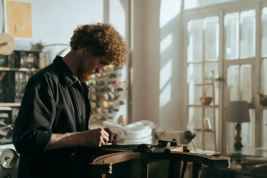 Atelier d'un artisan appliquant des clous de tapissiers sur la structure d'un fauteuil en cuir 