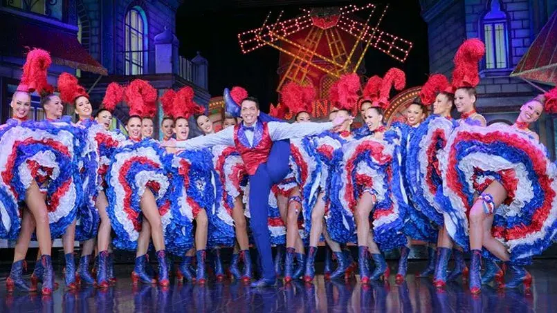 Des danseurs en tenue d'époque bariolée exécutent le mythique french cancan sur la scène du Moulin Rouge. 