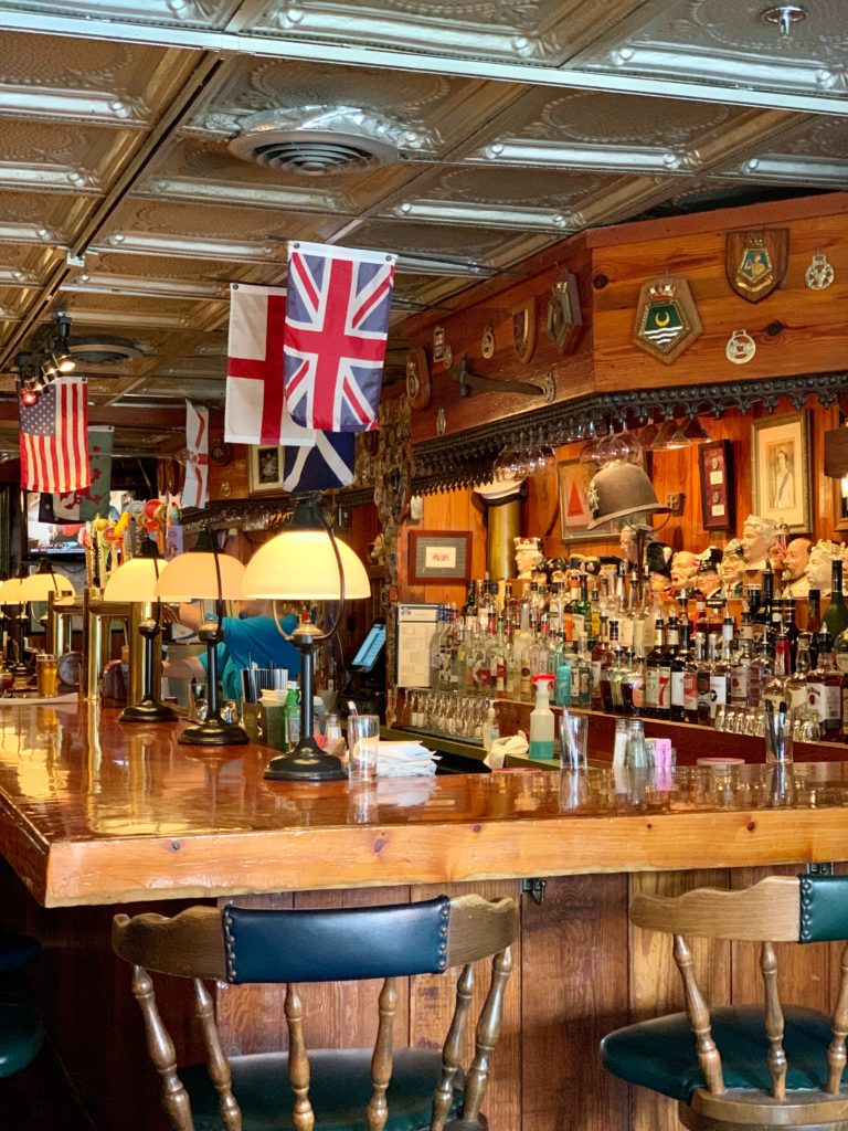 Intérieur typique d'un pub anglais avec drapeau britannique, bar et étagères en bois garnies de bouteilles d'alcools. 