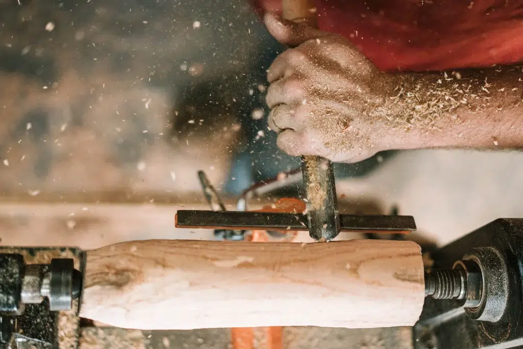 Gros plan sur des mains d'artisan en train de travailler la forme d'une pièce de bois clair 