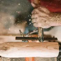 Gros plan sur des mains d'artisan en train de travailler la forme d'une pièce de bois clair