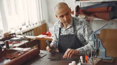 Artisan à l'œuvre sur sa table dans son atelier, travaille une pièce de cuir 